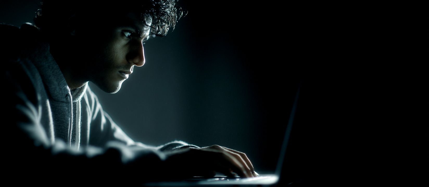 A man sits in the dark at his laptop with a focused expression on his face betting online at the BD33 website